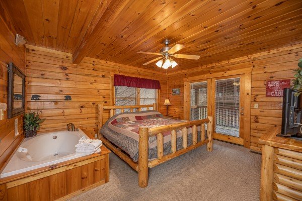 Bedroom with a king log bed, jacuzzi, dresser, and deck access at Alpine Tranquility, a 4 bedroom cabin rental located in Pigeon Forge