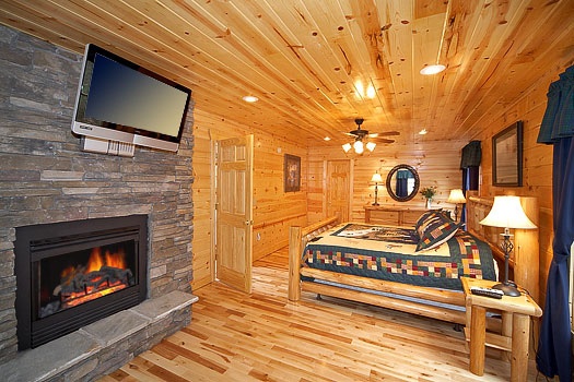 King-sized bed with stone fireplace and flat screen tv in master bedroom at Big Bear Falls, a 2-bedroom cabin rental located in Gatlinburg