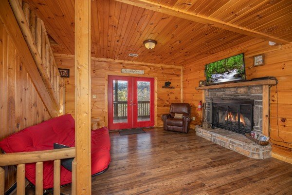 Lower living room with futon, fireplace, TV, and deck access at Wonders in the Sky, a 3 bedroom cabin rental located in Gatlinburg