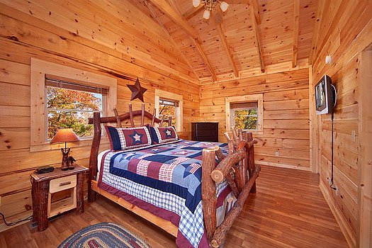 King sized log bed with TV mounted to wall at foot of bed at Looky Yonder, a 2 bedroom cabin rental located in Gatlinburg