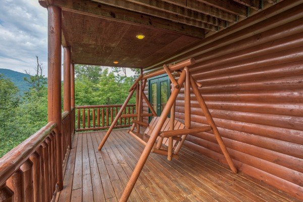 A log porch swing on a covered deck at Horse'n Around, a 3 bedroom cabin rental located in Pigeon Forge