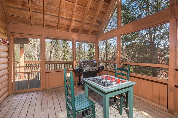 Screened-in porch with  a checker game and propane grill at Golden Memories, a 1-bedroom cabin rental located in Pigeon Forge