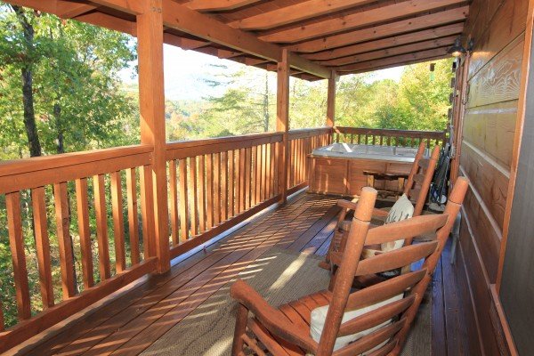 Rocking chairs and hot tub on a covered deck at Bear Hug Hideaway, a 1-bedroom cabin rental located in Pigeon Forge