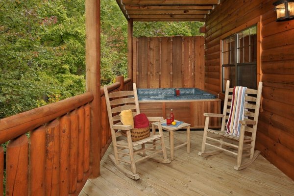 Hot tub with privacy fence and wooded views near two rocking chairs at Family Ties Lodge, a 4-bedroom cabin rental located in Pigeon Forge