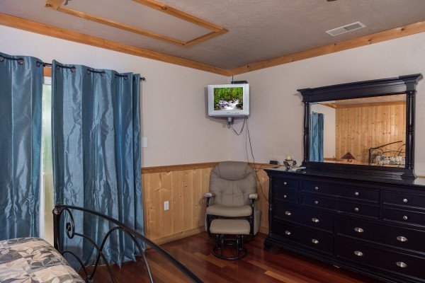 Bedroom with a glider rocker, corner-mounted television, and dresser with mirror at Breezy Mountain Lodge, an 11-bedroom cabin rental located in Pigeon Forge