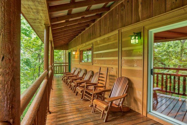 Six Adirondack chairs and a rocking chair on the covered deck at Breezy Mountain Lodge, an 11-bedroom cabin rental located in Pigeon Forge
