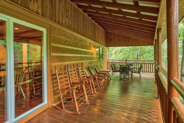 Three rocking chairs, three Adirondack chairs, and a dining table on the covered deck at Breezy Mountain Lodge, an 11-bedroom cabin rental located in Pigeon Forge
