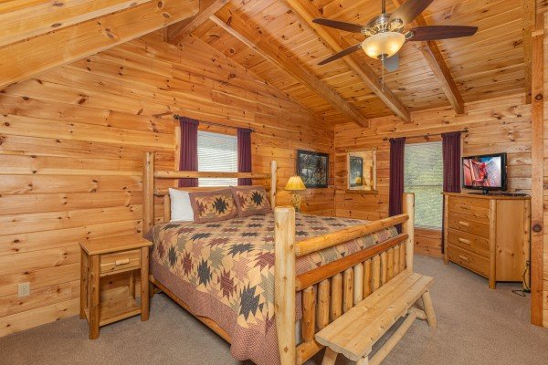 King log bed, bench, dresser, and TV in a bedroom at Smokies Paradise Lodge, a 5 bedroom cabin rental located in Pigeon Forge