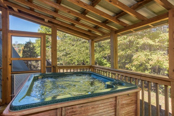 Hot tub on a covered screened porch at Living on Love, a 2 bedroom cabin rental located in Pigeon Forge