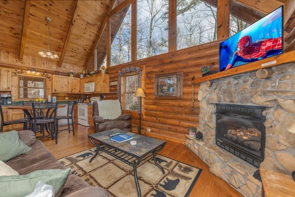 Living room with fireplace and TV attached to a dining space and kitchen at A Lover's Secret, a 1 bedroom cabin rental located in Gatlinburg