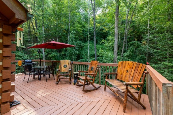 Rocking chairs, bistro table, and bench on the deck at Cabin by the Creekside, a 4 bedroom cabin rental located in Pigeon Forge