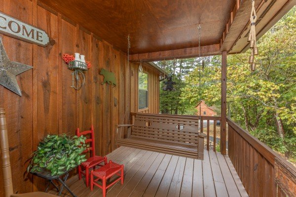 Porch swing and plants on a covered deck at Black Bear Holler, a 2 bedroom cabin rental located in Pigeon Forge