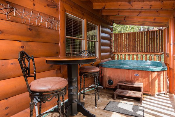 Bar top table with seating for two and hot tub on a covered deck at Bearfoot Memories, a 2-bedroom cabin rental located in Pigeon Forge