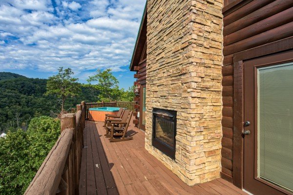Fireplace, rocking chairs, and hot tub on a deck at Majestic Views, a 3 bedroom cabin rental located in Pigeon Forge